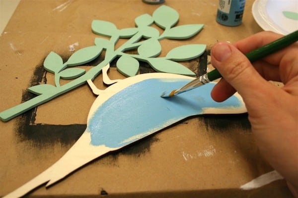 maling af et træstykke med lyseblå håndværksmaling ved hjælp af en pensel
