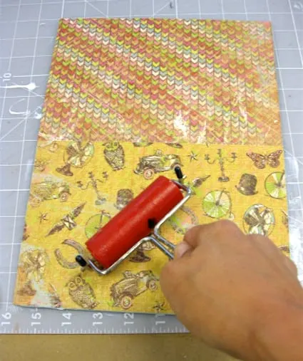 Using a brayer to smooth the scrapbook paper over the Mod Podge