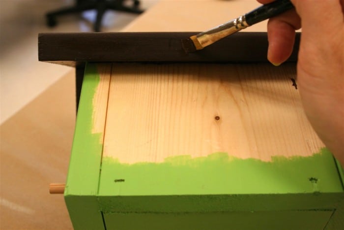 Painting the birdhouse around the edges with green and on the roof with brown