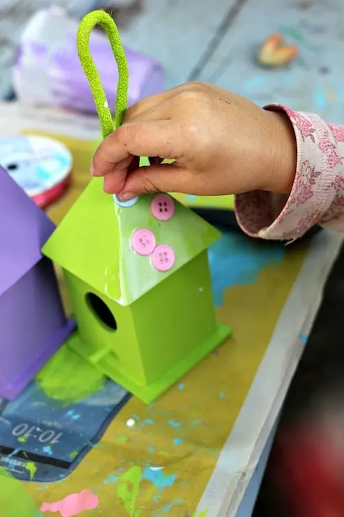 Glueing buttons onto the birdhouse with Mod Podge