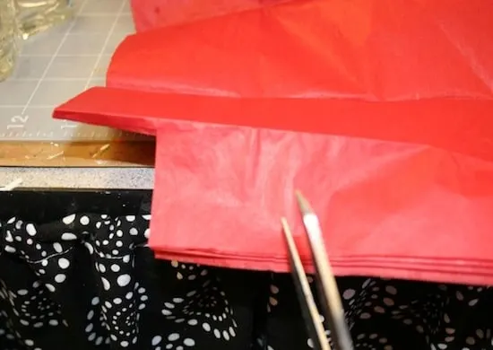 Cutting red tissue paper with scissors