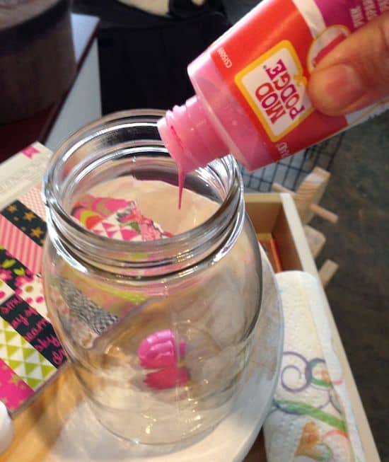 Squeezing pink colored Mod Podge into a mason jar