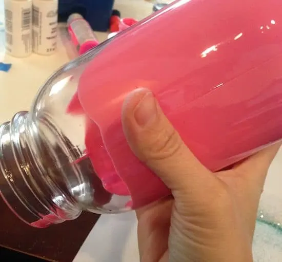 Hand turning a mason jar with colored Mod Podge inside