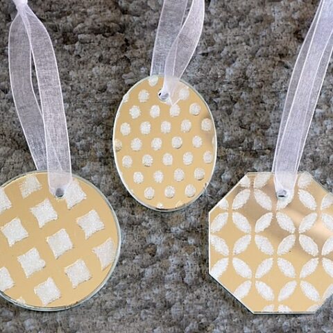 Use white glitter and Mod Podge Rocks stencils to make these pretty and simple DIY ornaments out of mirrors.