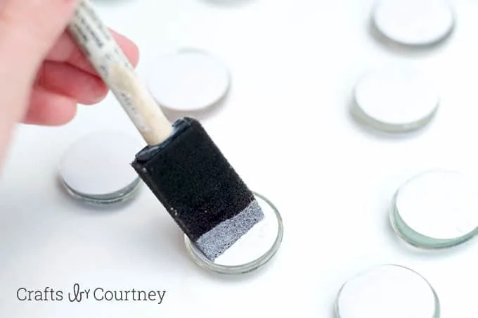 Painting Mod Podge on the back of marble magnets with a foam brush