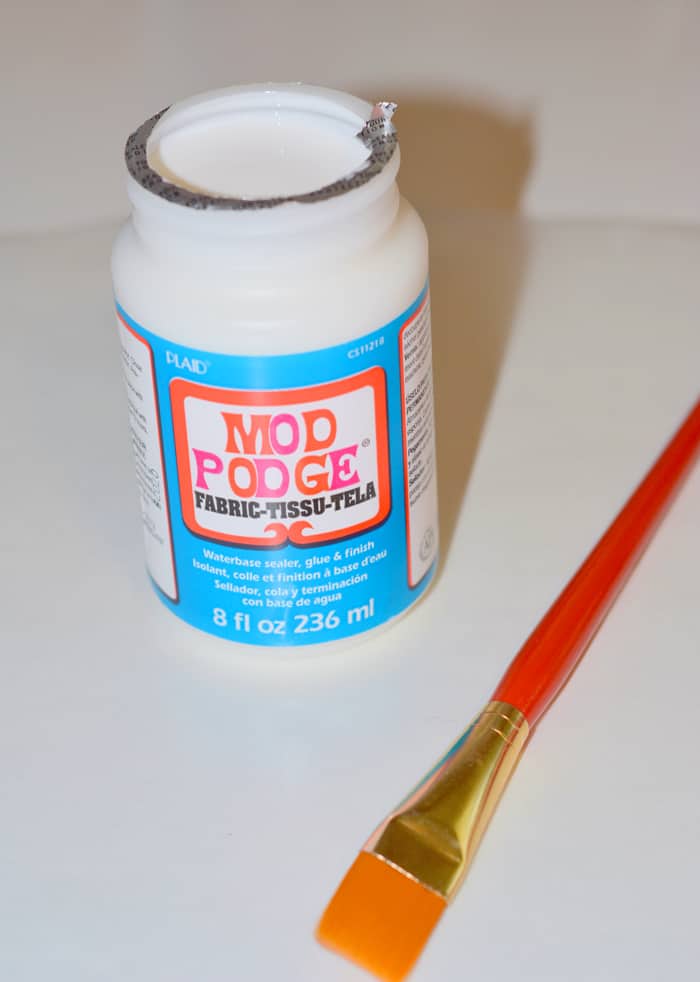 Bottle of Mod Podge Fabric with a paintbrush laying in front of it