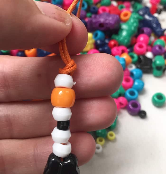 Stringing white and black and orange beads onto orange thread