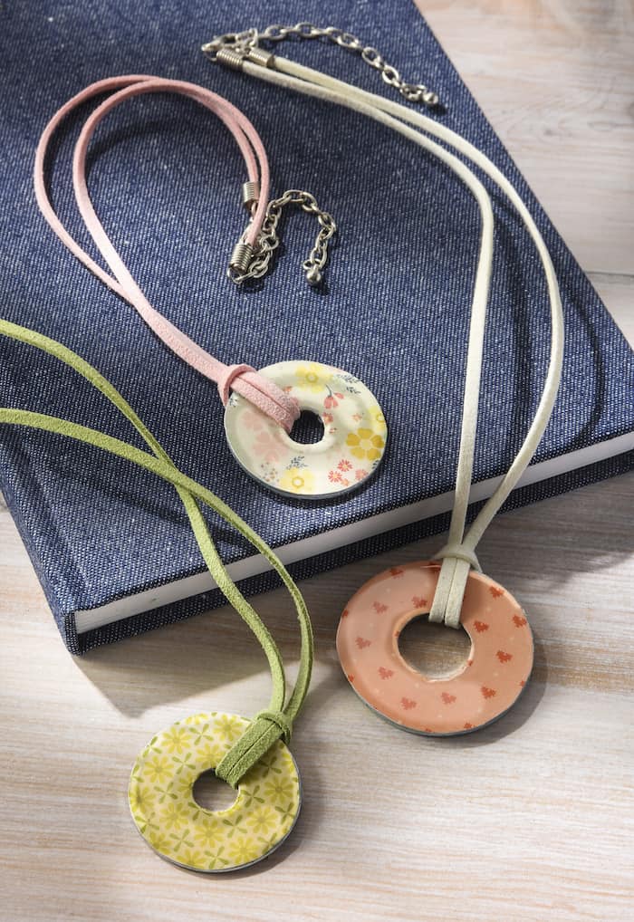 Three pastel washers with prints on leather strings laying on a denim covered book. 