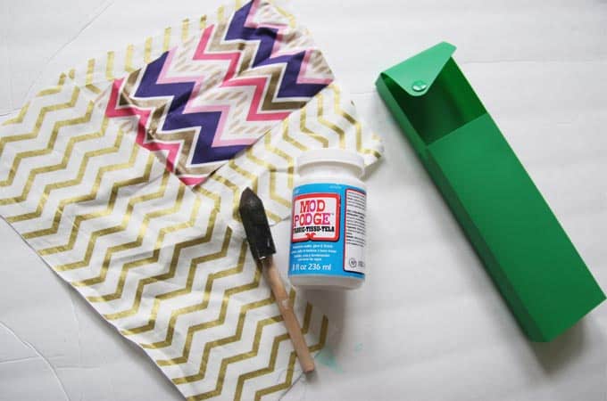 Fabric pieces, plastic pencil case, Mod Podge, and a foam brush