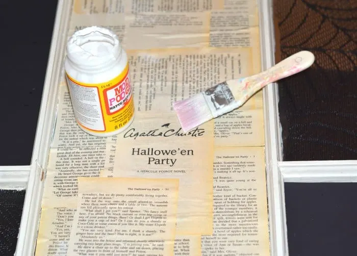 Painting Mod Podge on a book pages on a window pane