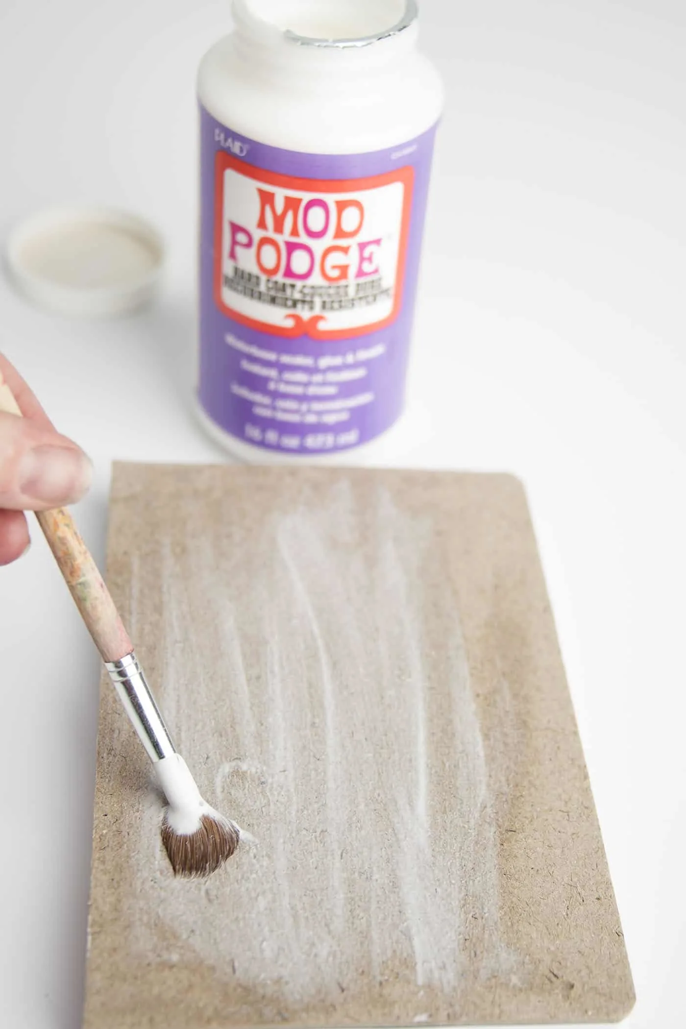 Paint Mod Podge on a paper mache sketchbook with a paint brush