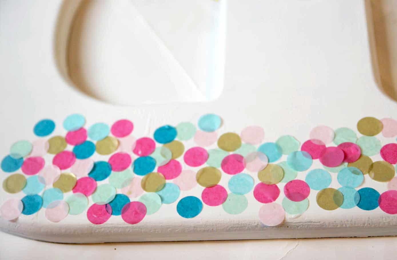 Colorful confetti being applied to a wood surface with Mod Podge