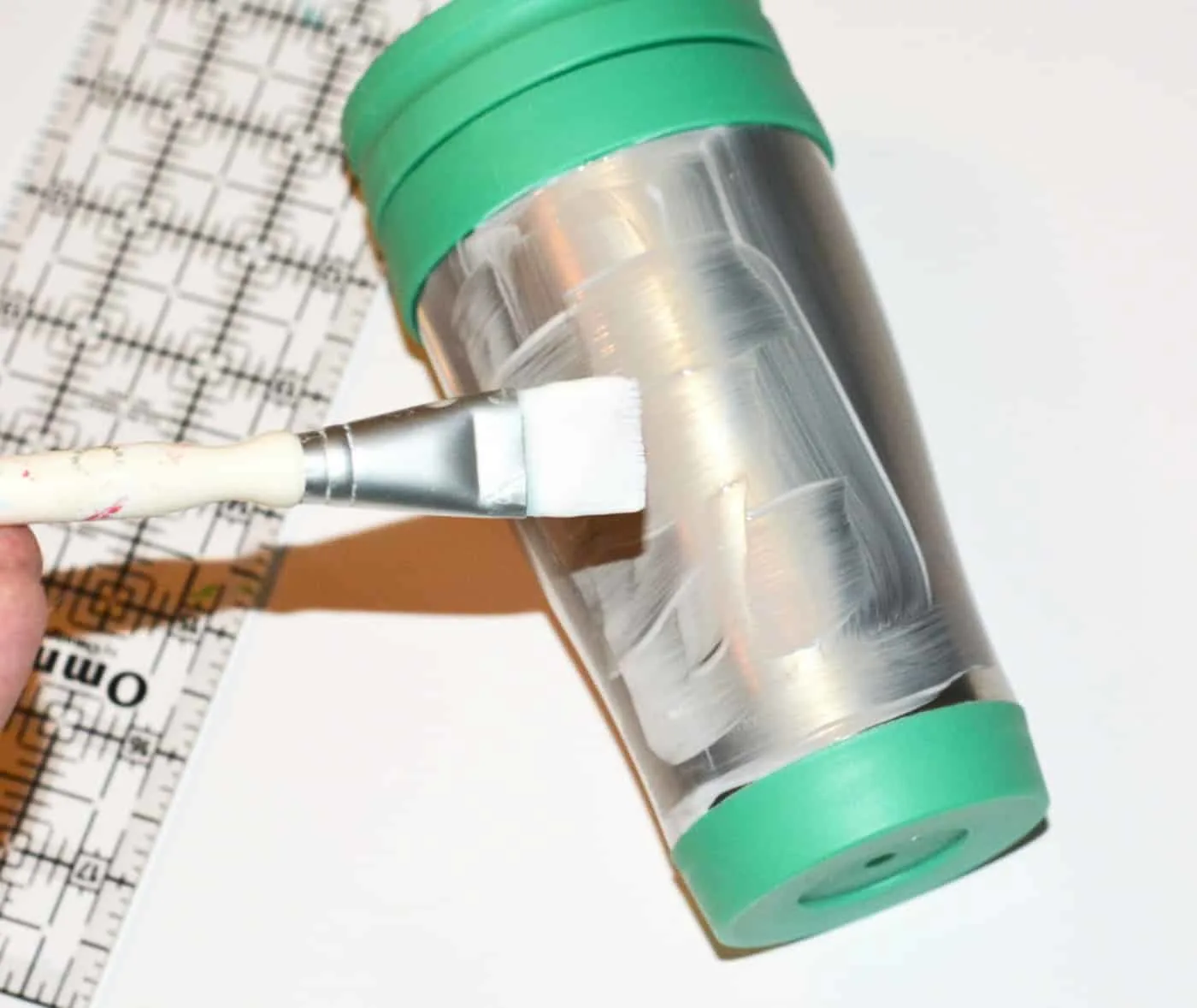 Painting Mod Podge Dishwasher Safe onto the side of a travel mug with a paintbrush