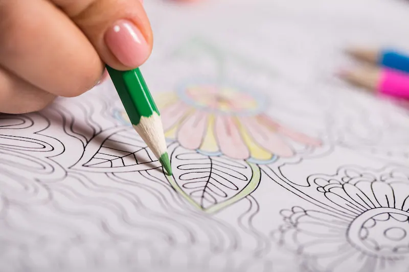 Girl paints a coloring book for adults with crayons