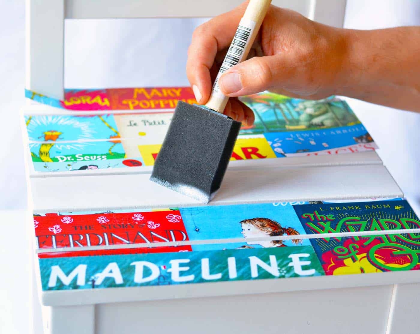 Applying book cover images to the top of a chair with Mod Podge and a foam brush