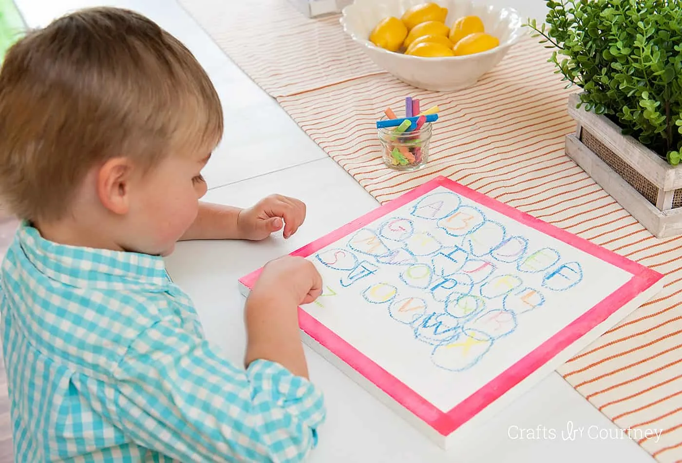 Child using colored chalk on top of a white chalkboard