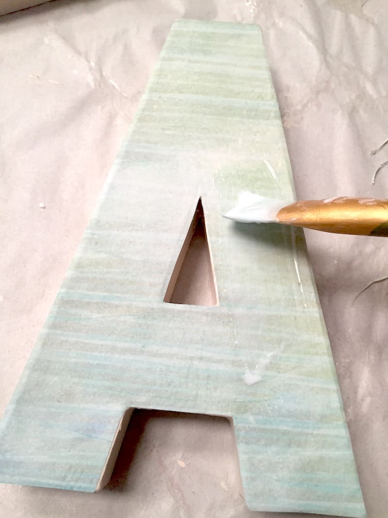 Applying Mod Podge to the top of the paper on the letters with a paintbrush