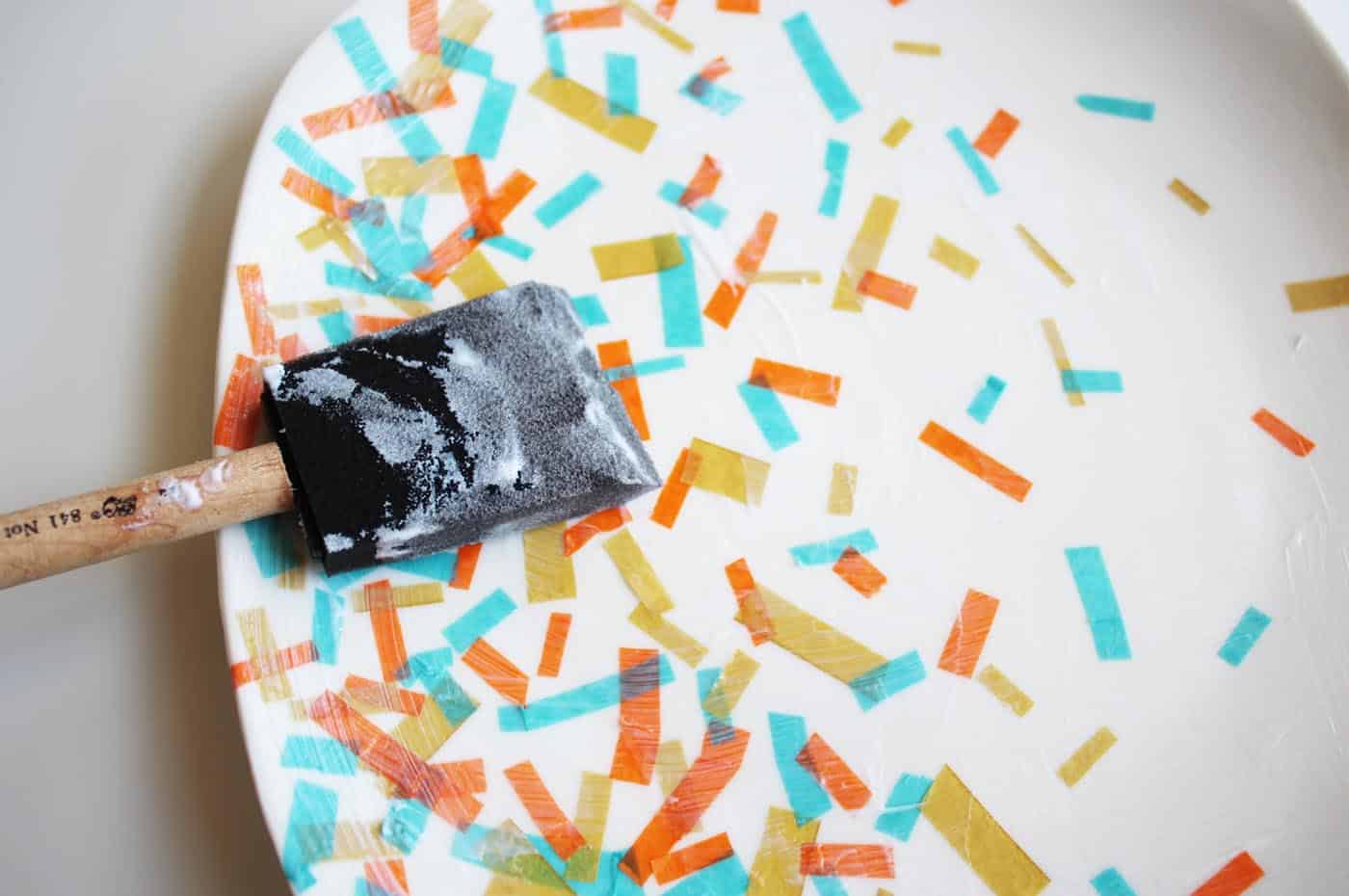 Brushing a layer of Dishwasher Safe Mod Podge over confetti on a dollar store plate