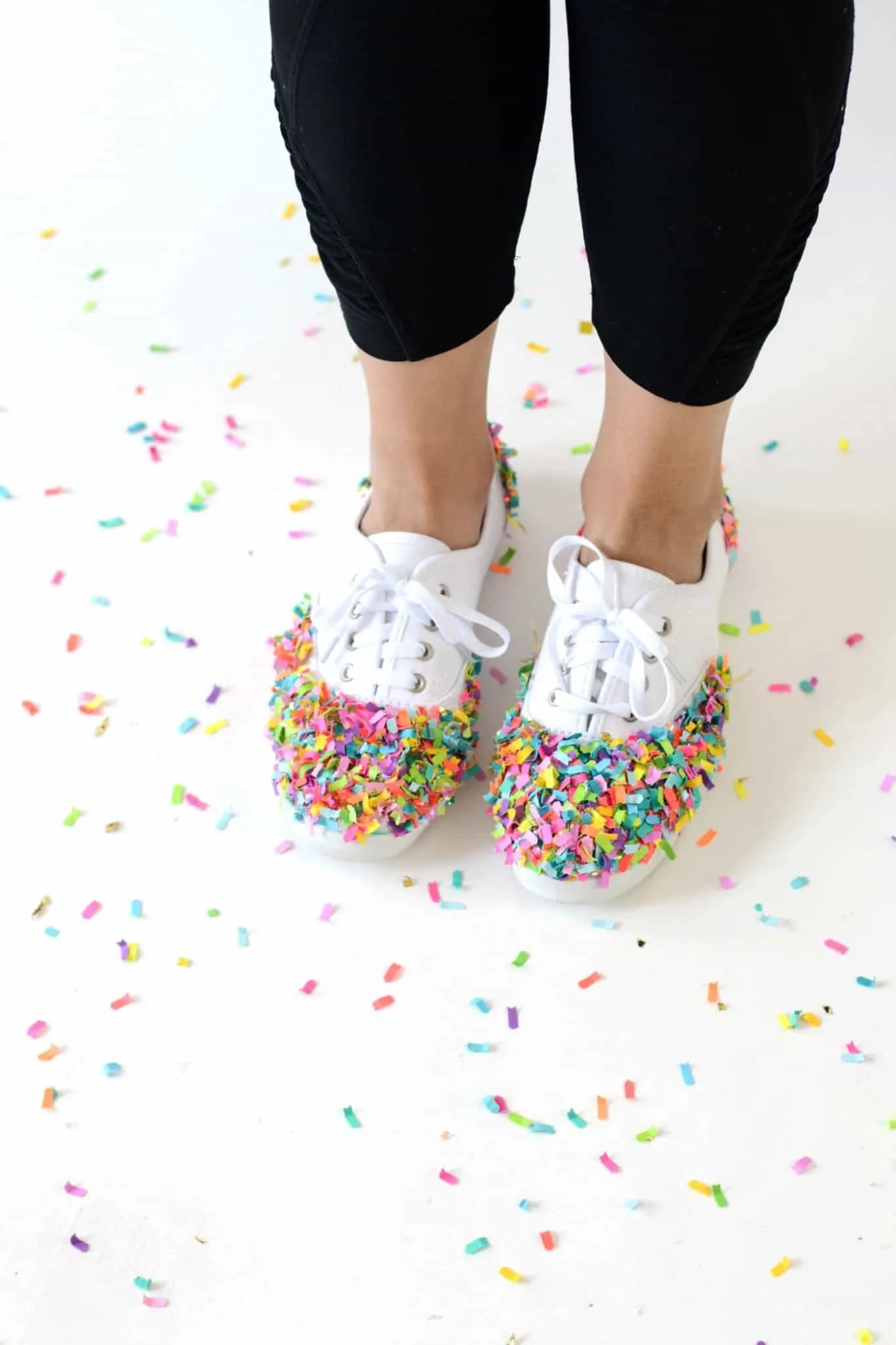 Woman wearing white tennis shoes covered in colorful confetti