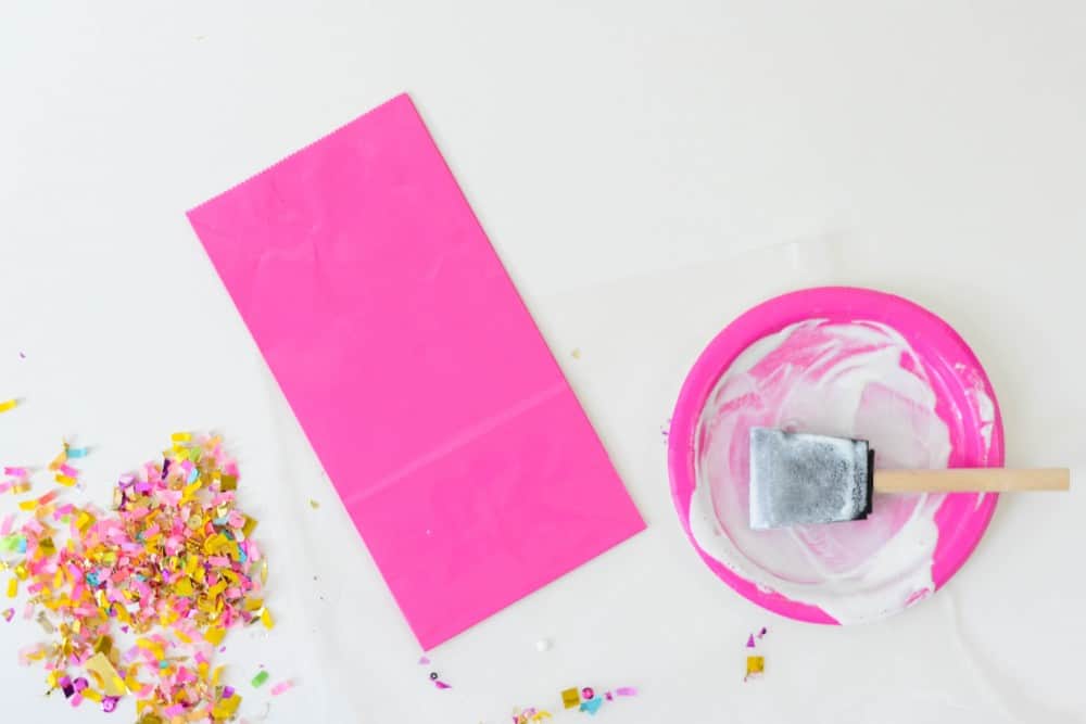 Pink favor bag with confetti and a foam brush sitting in Mod Podge