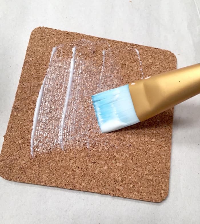 Applying Mod Podge to a cork coaster with a paintbrush