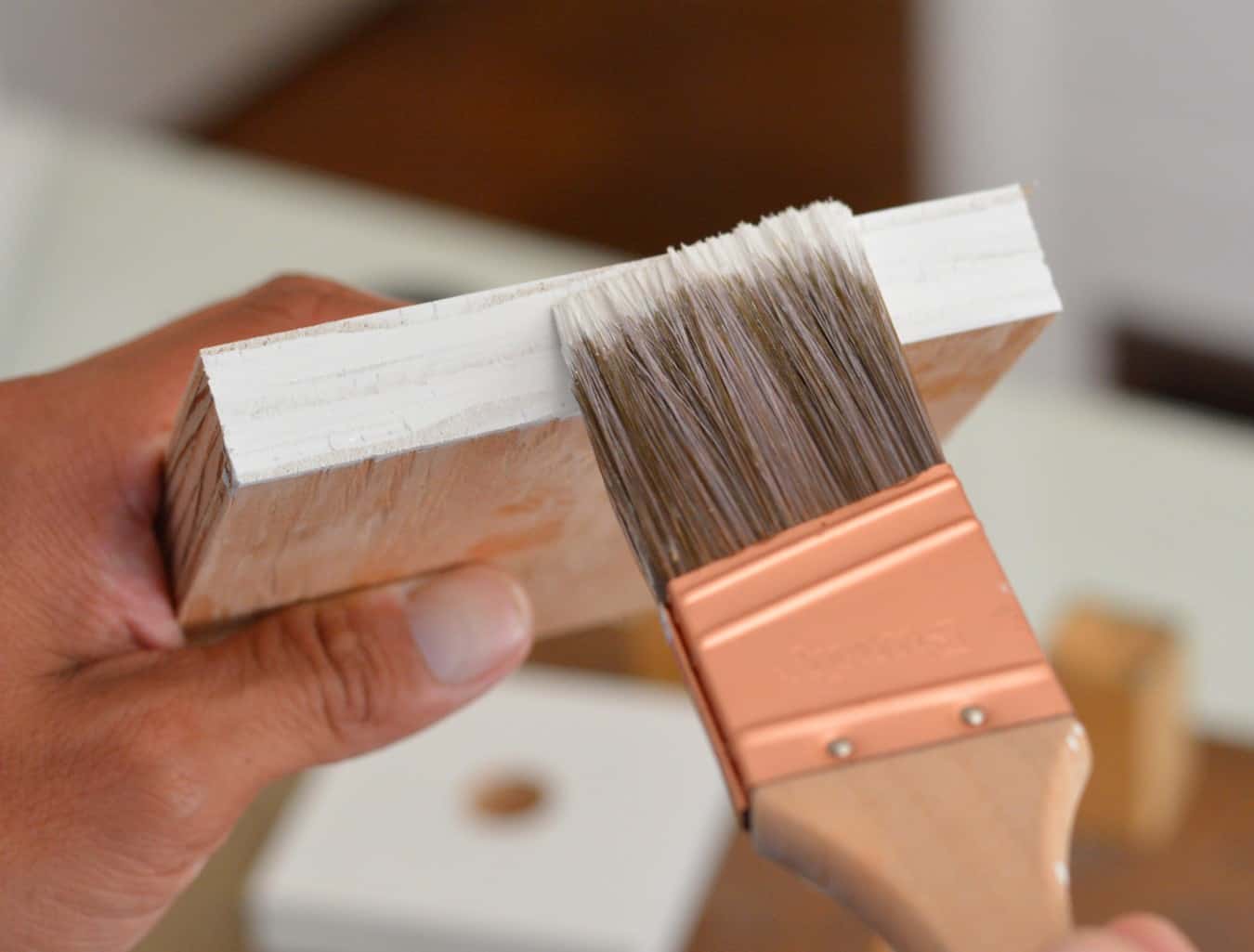 Painting the edge of a piece of wood with white paint using a paint brush