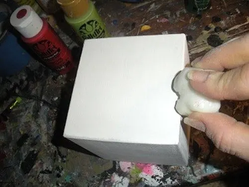 Rubbing a piece of wax on a wood block painted with white acrylic paint
