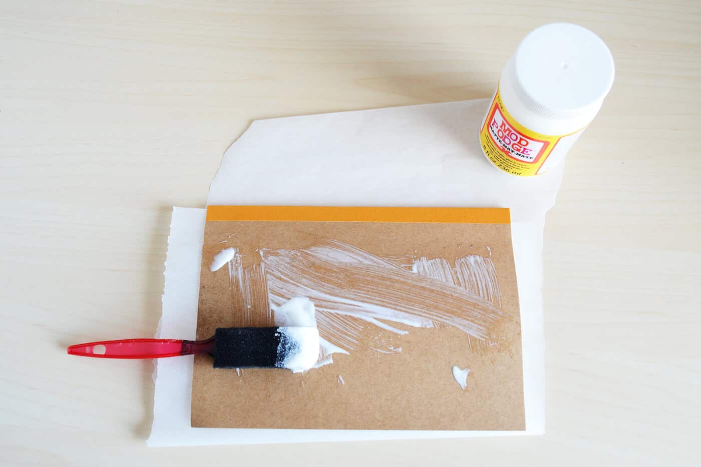 Applying Mod Podge to a notebook cover with a foam brush