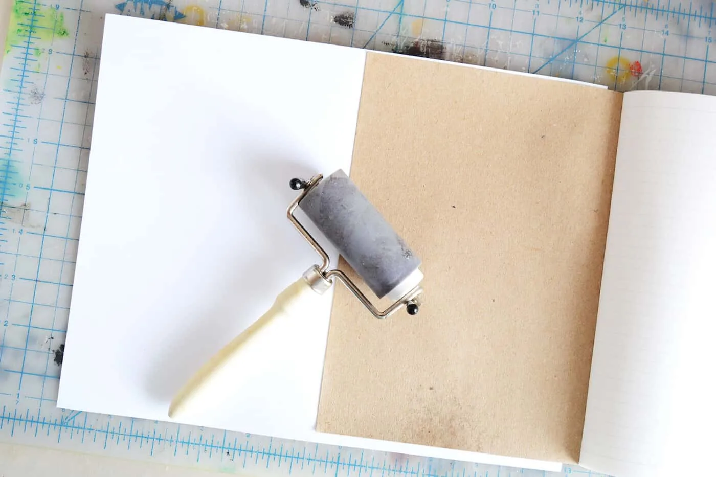 Using a brayer to adhere the paper to the notebook cover