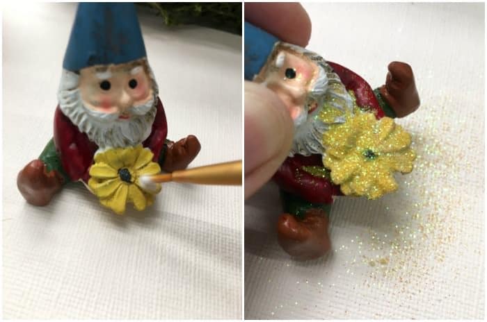Adding Mod Podge to a gnome with a yellow flower and then sprinkling glitter on top