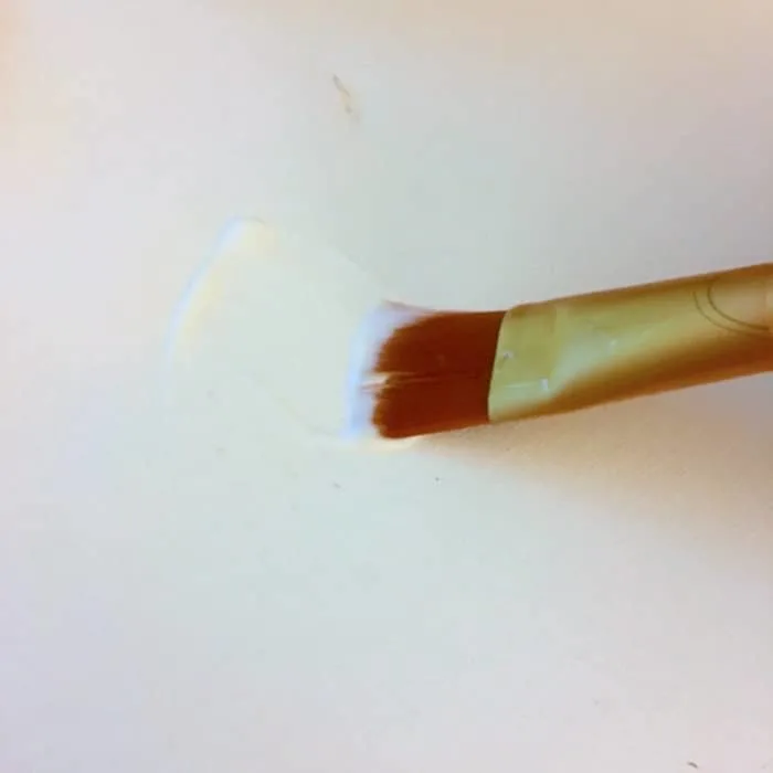 Applying Mod Podge to a canvas with a paintbrush