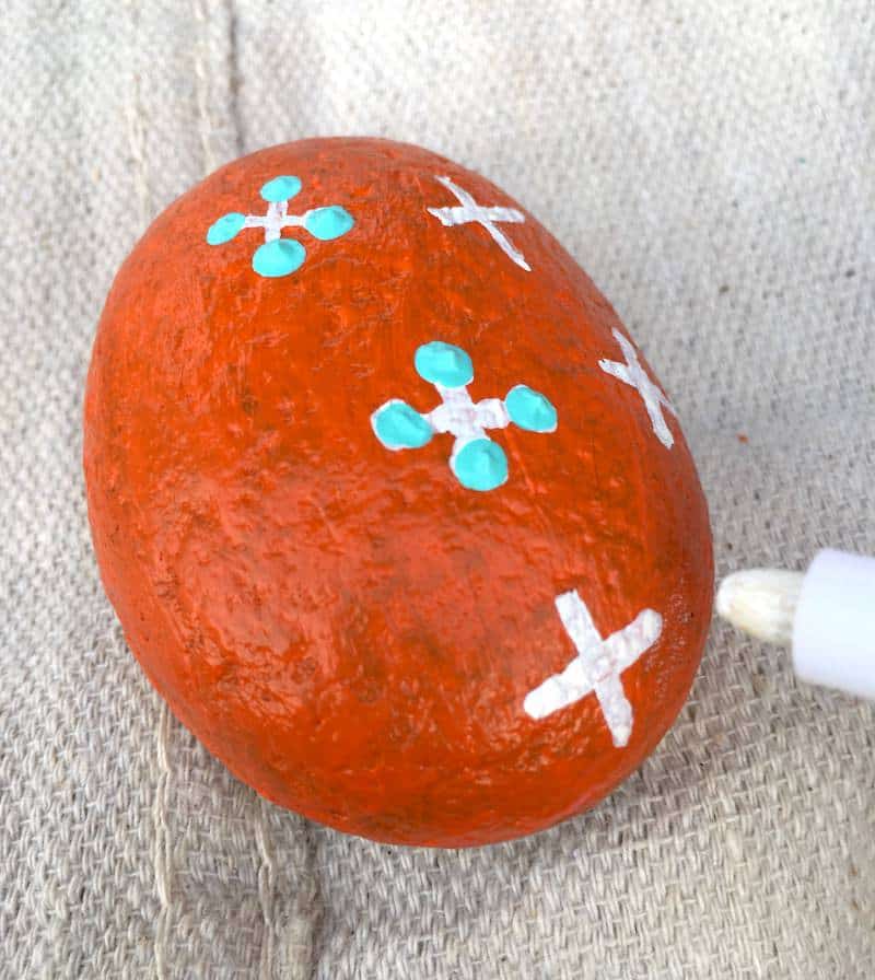 Kindness Rock Project - orange painted rock with white Xs and aqua blue dots