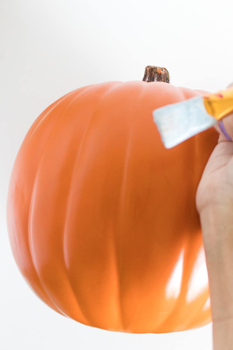 Applying Mod Podge to a faux pumpkin with a paintbrush