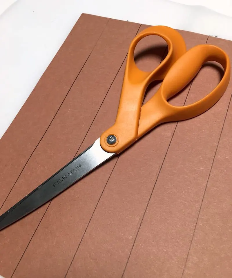 Brown construction paper with lines drawn on it and a pair of orange handled scissors