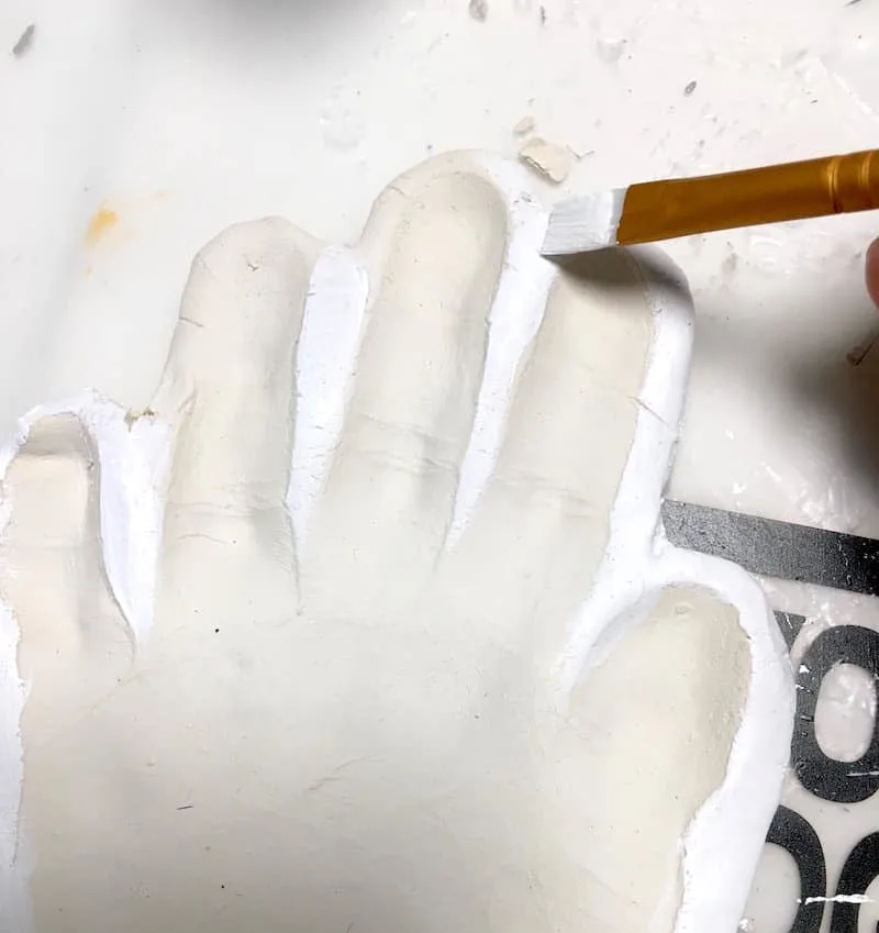 Painting the edge of a child's handprint with white acrylic paint