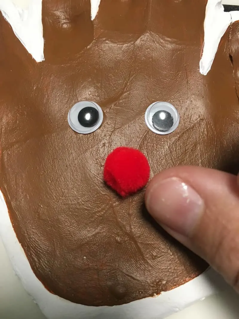Gluing a pom pom nose on a Christmas reindeer handprint