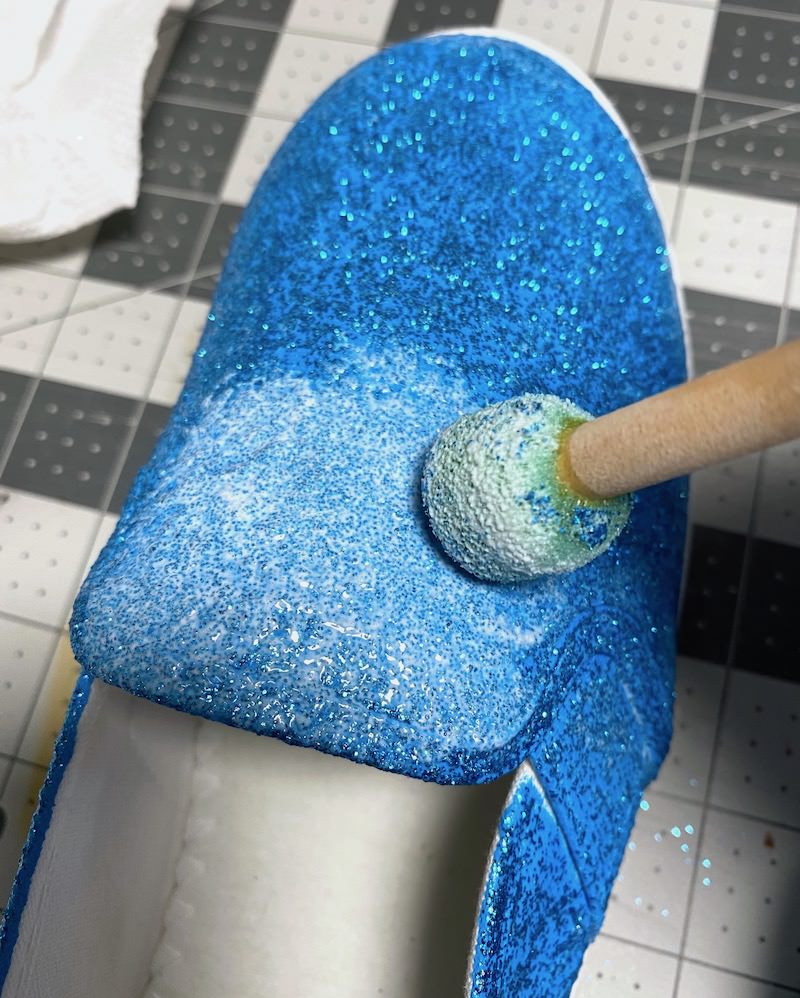 Applying a second coat of Mod Podge and glitter to a shoe with a spouncer