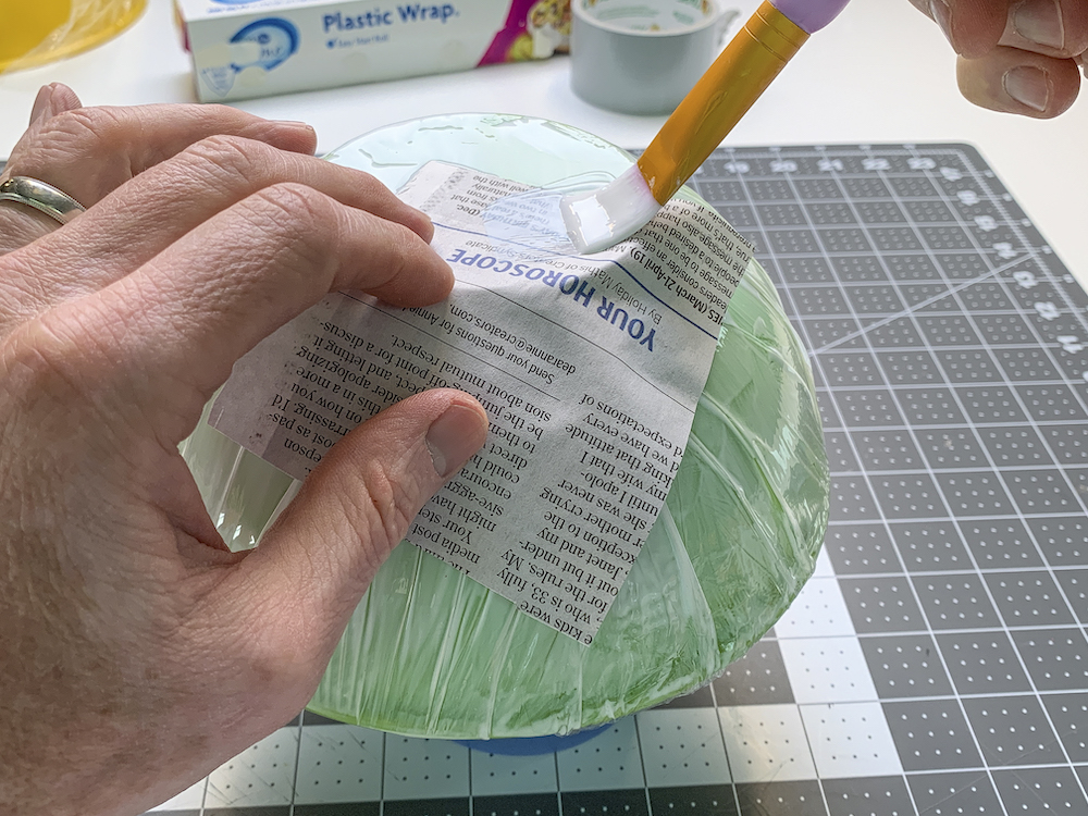 Applying newspaper to a bowl with Mod Podge