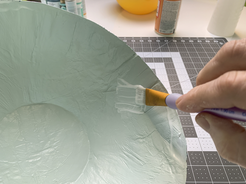 Finishing painting a paper mache bowl with paint