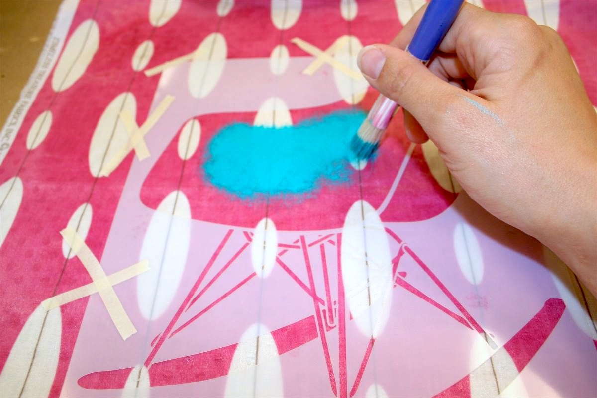 Using aqua paint to stencil a mid century modern chair on the fabric