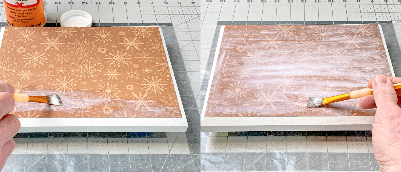Pintando uma camada de Mod Podge por cima do papel na placa de madeira
