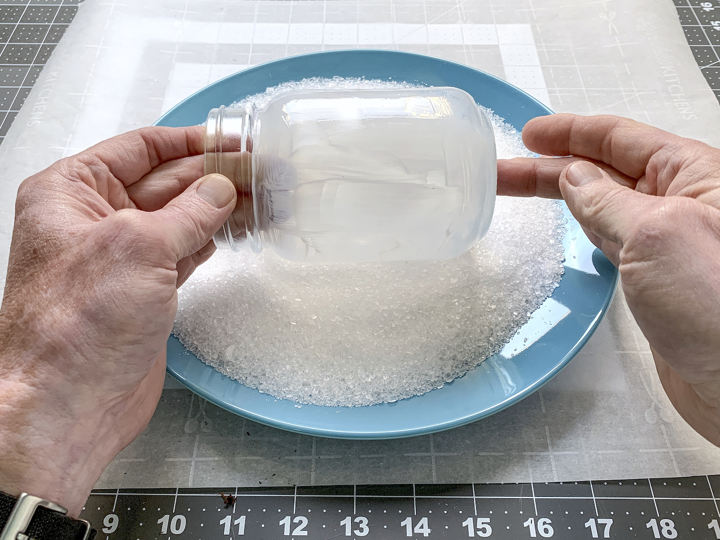 Mãos enrolando um frasco de vidro coberto de Mod Podge em sal de Epsom