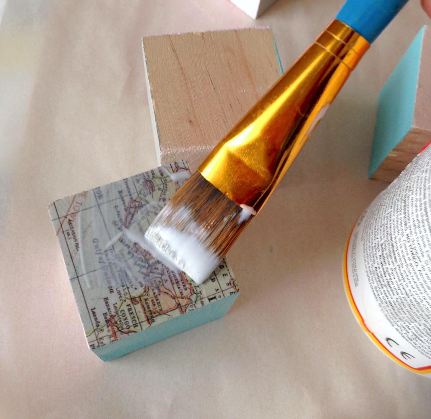 Mod Podge a wooden block with a paintbrush