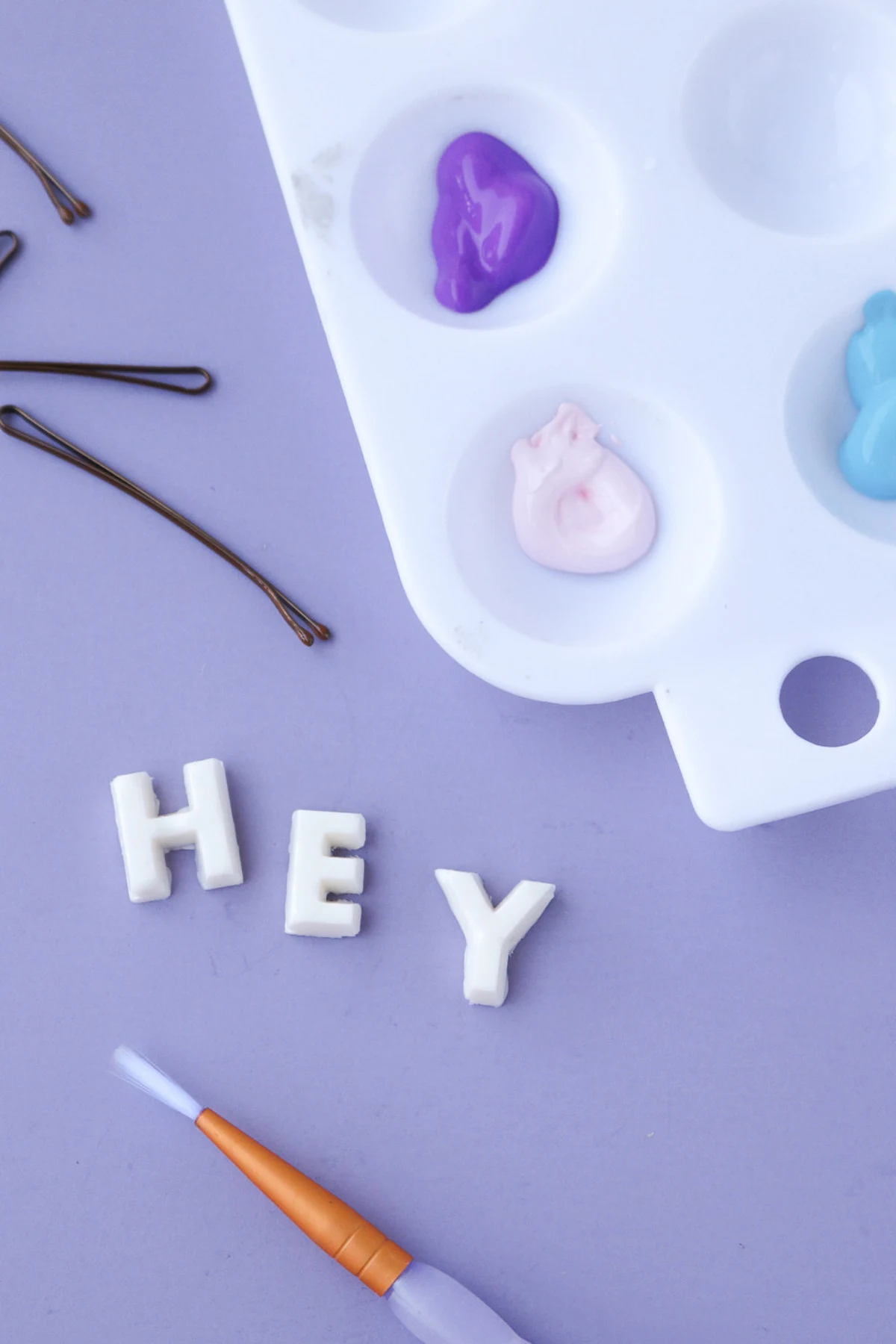 hot glue letters that spell HEY with pink paint in a tray and a brush
