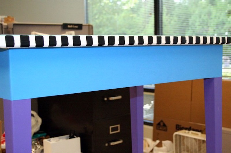 Black stripes painted on the edge of a tabletop with a blue base and purple legs