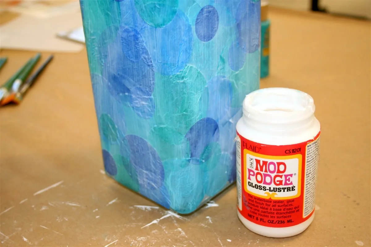 Mod Podge over the top of tissue paper with a bottle of Mod Podge sitting next to it