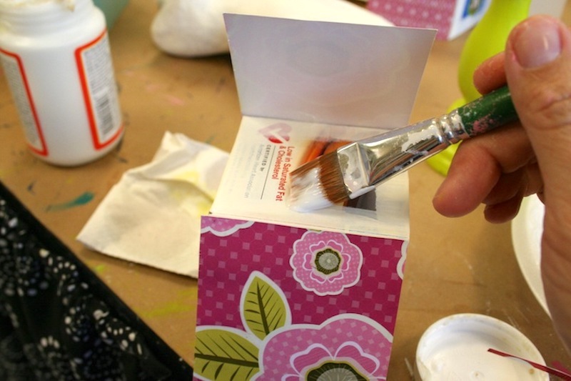 Painting Mod Podge on a cereal box to fold down the paper