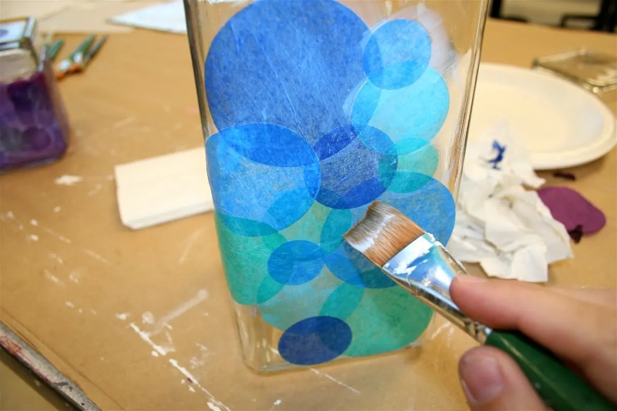 Painting Mod Podge onto the tissue paper on the glass jar