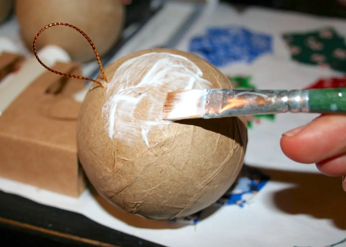 Applying Mod Podge to a paper mache ornament with a paintbrush