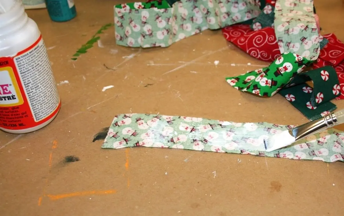 Applying Mod Podge to a strip of Christmas fabric